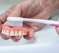 a person brushing their dentures over the sink