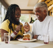 Couple smiling while eating slice of cake together