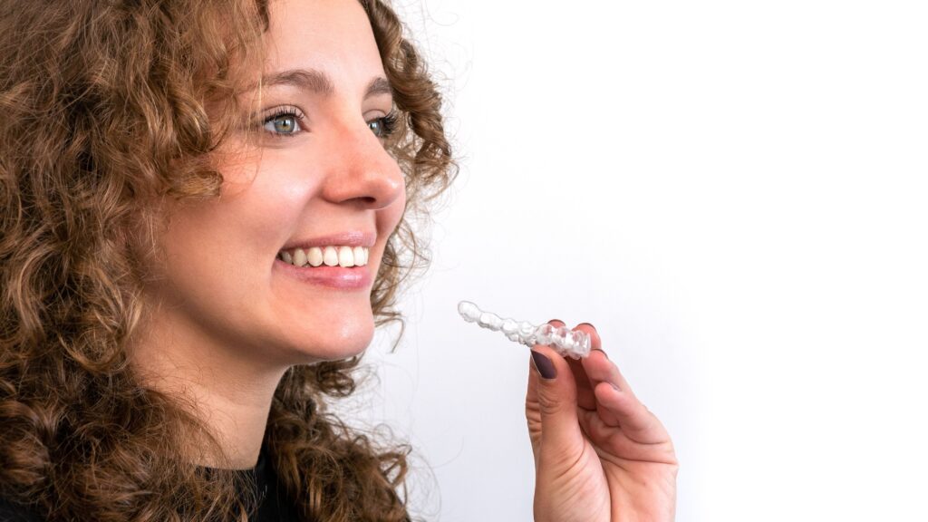 An adult woman holding a SureSmile clear aligner.